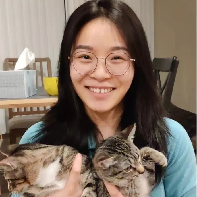 Smiling young woman with glasses holding two tabby cats in her arms.